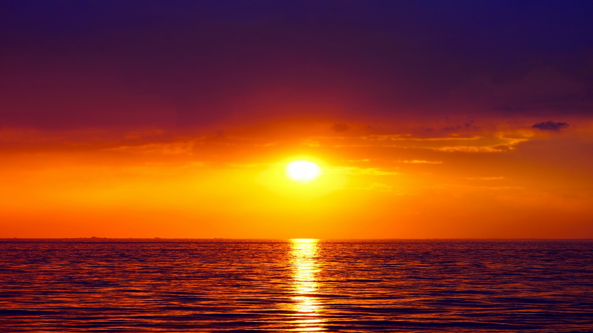Un soleil doré se couche sur la mer sous un ciel violet et orangé